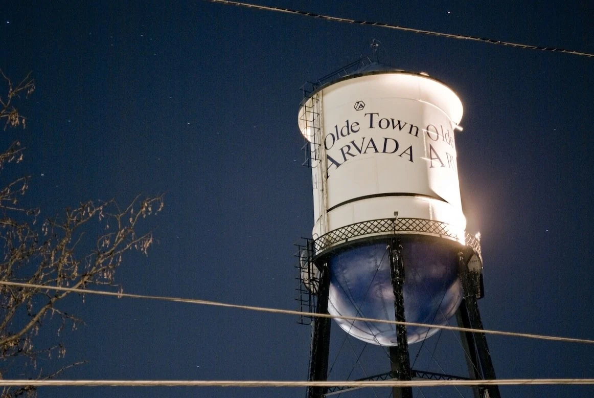Illuminated Olde Town Arvada water tower against the evening sky
